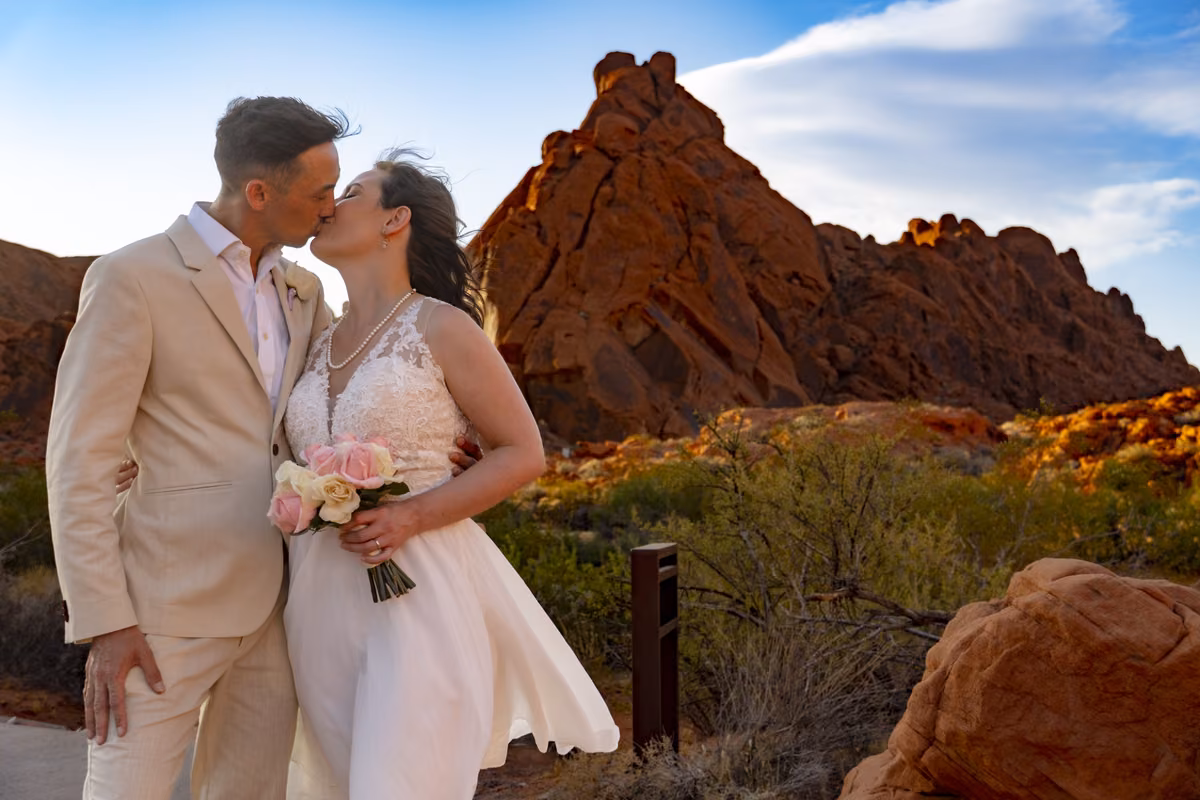 Newlyweds kiss in front of jagged red rock peaks under a blue sky at Valley of Fire State Park.