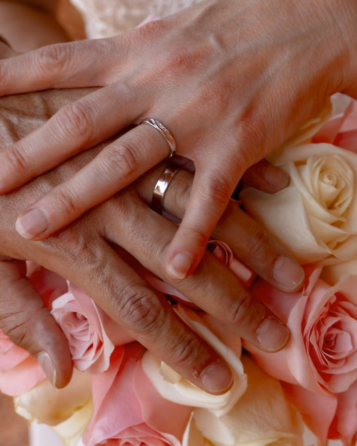 Wedding rings on the couple's hands resting on a pink and ivory rose bouquet after their Valley of Fire ceremony.